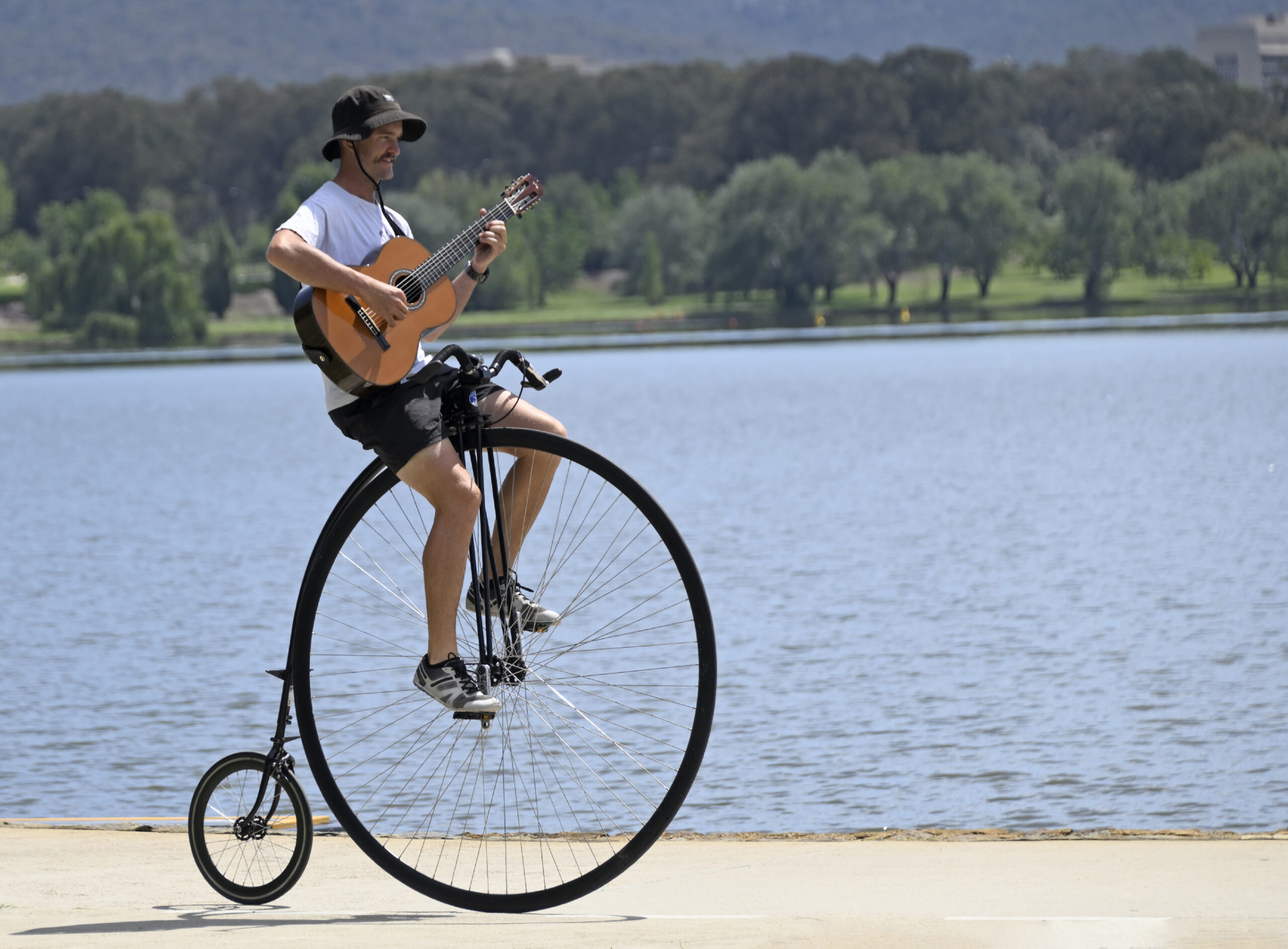 Simon playing his guitar while riding his penny-farthing